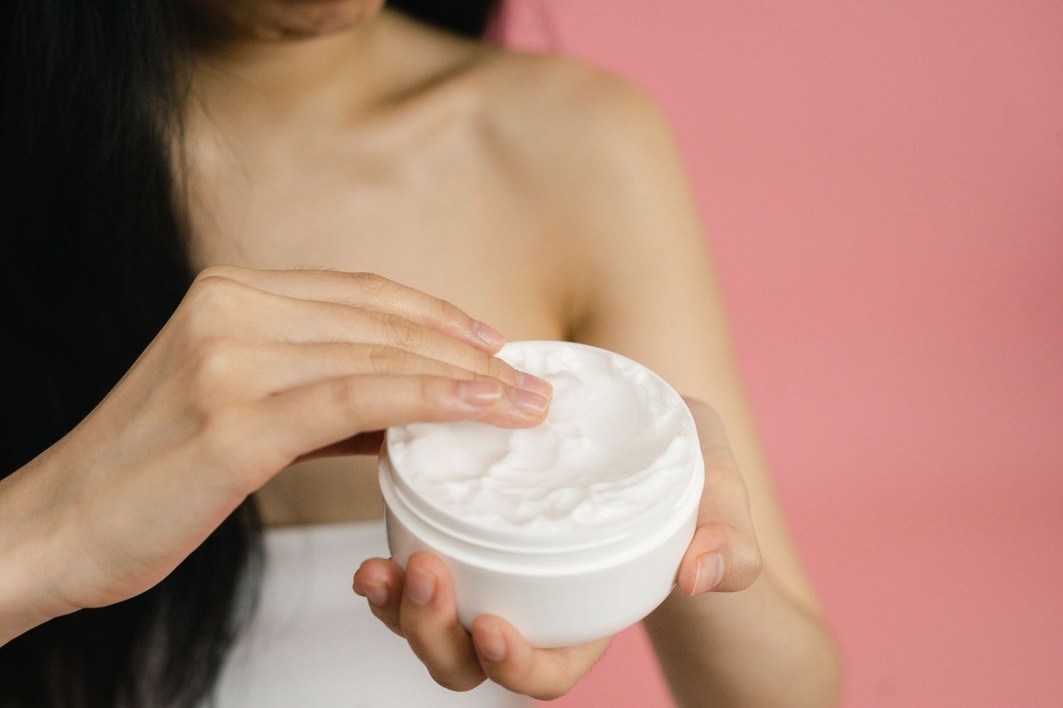 女性手持白色乳霜罐,準備塗抹保養